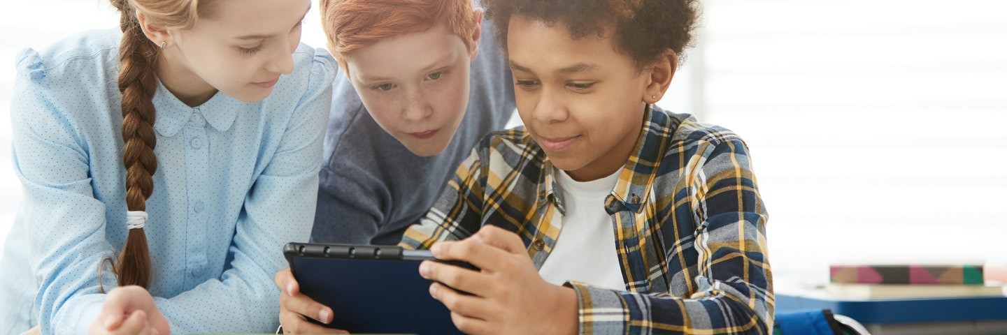 Three middle school children, two boys and one girl, look at a tablet while playing Prodigy Math Game.