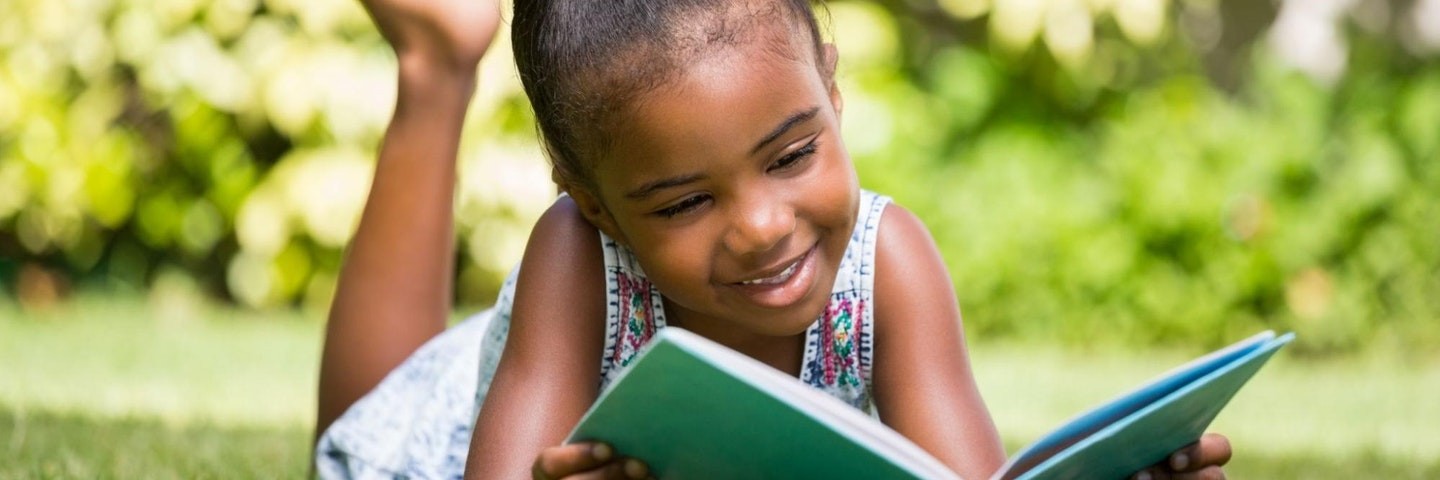 Young girl reads outside as part of a summer reading program. 