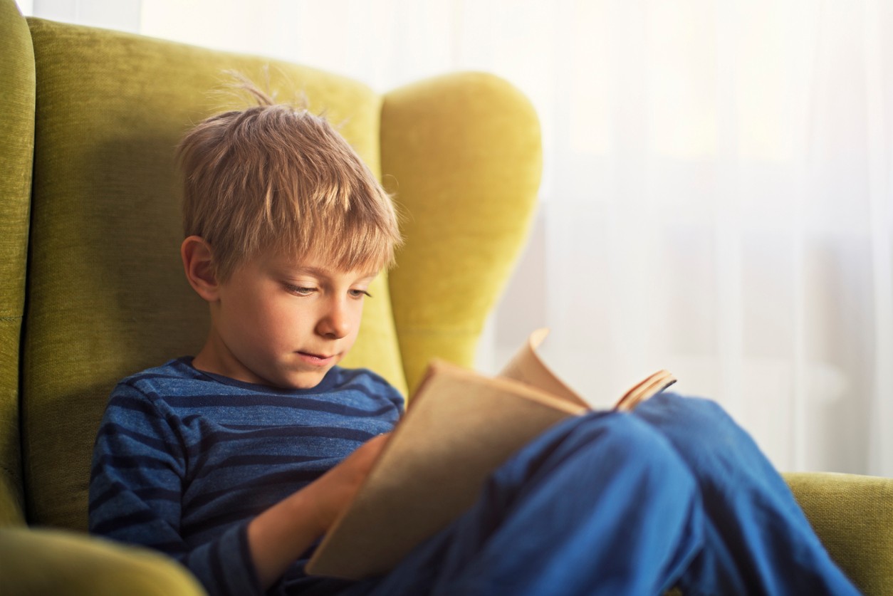 Child reading a book from his reading log in an armchair.