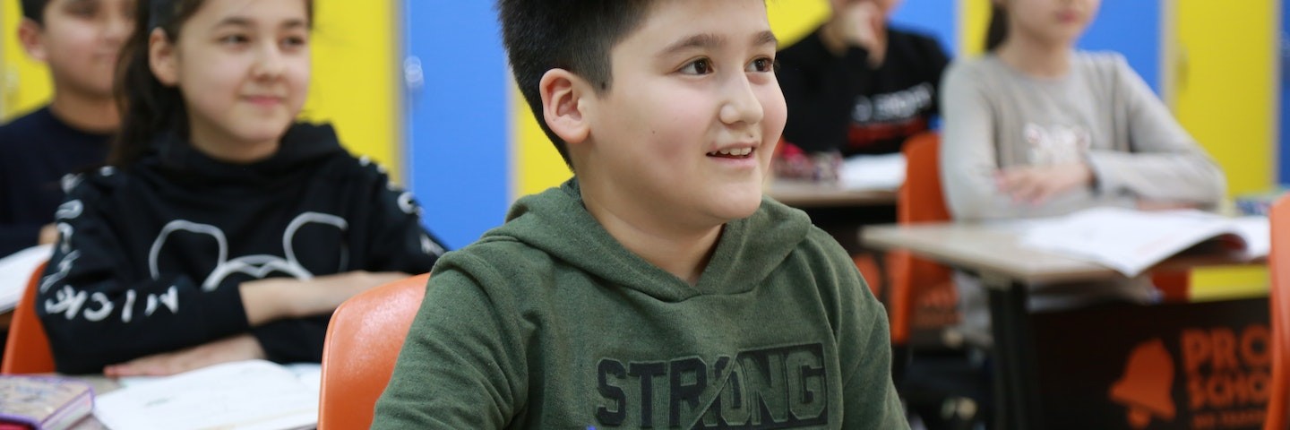 A group of five elementary students learning in class and smiling.