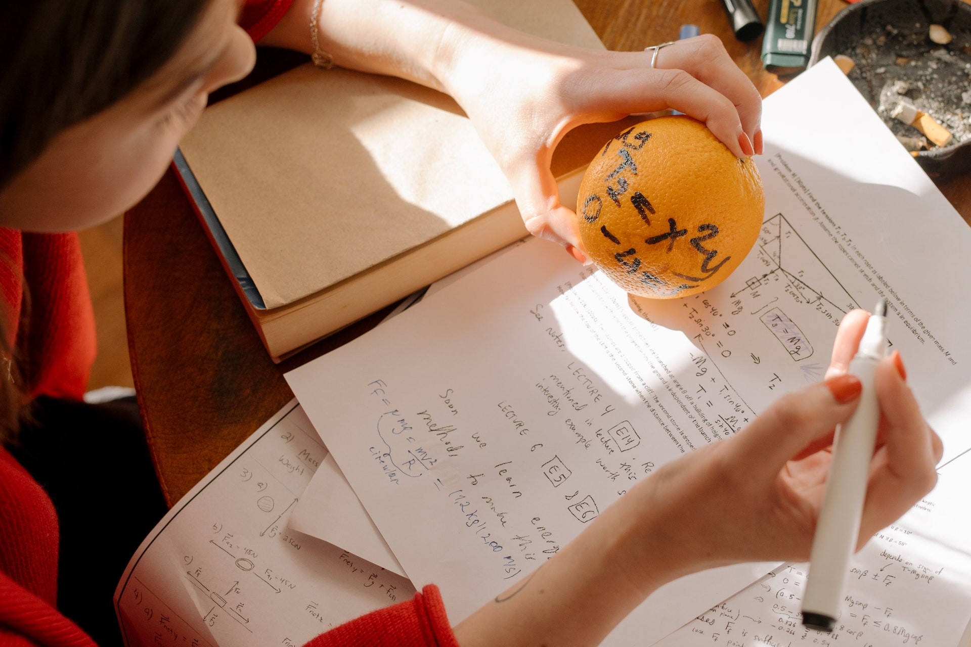 A student holds an orange with an equation written on it while working on a math writing prompt.