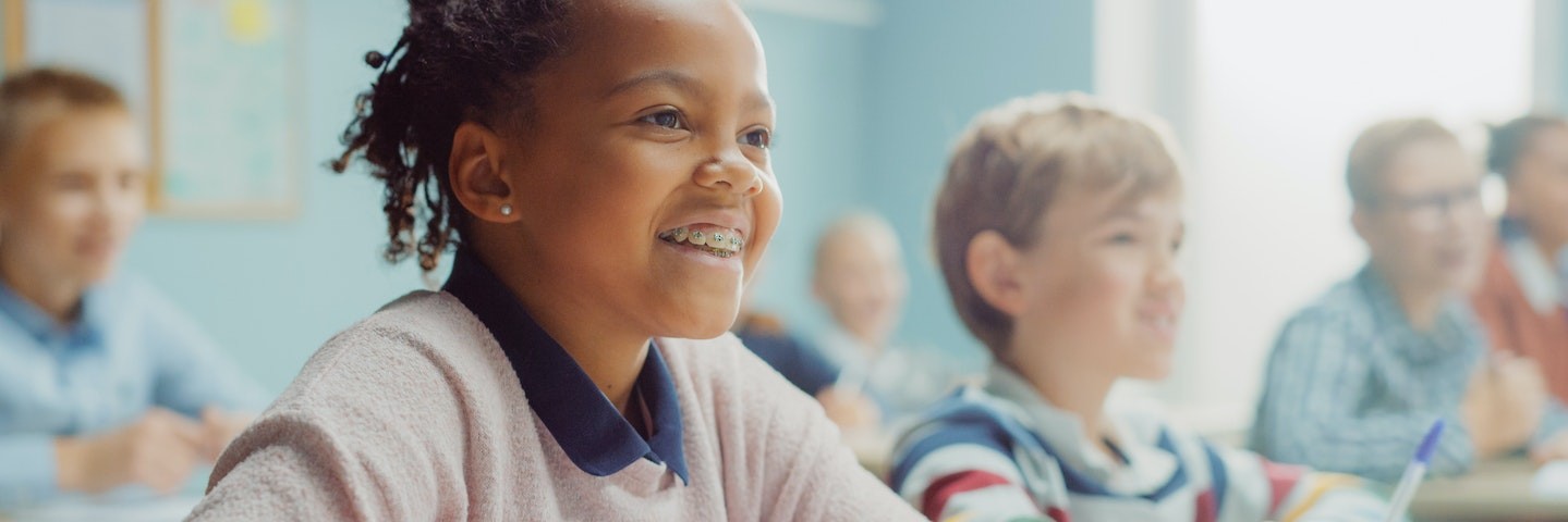 Young girl sits in a classroom smiling as she learns how to do long division.