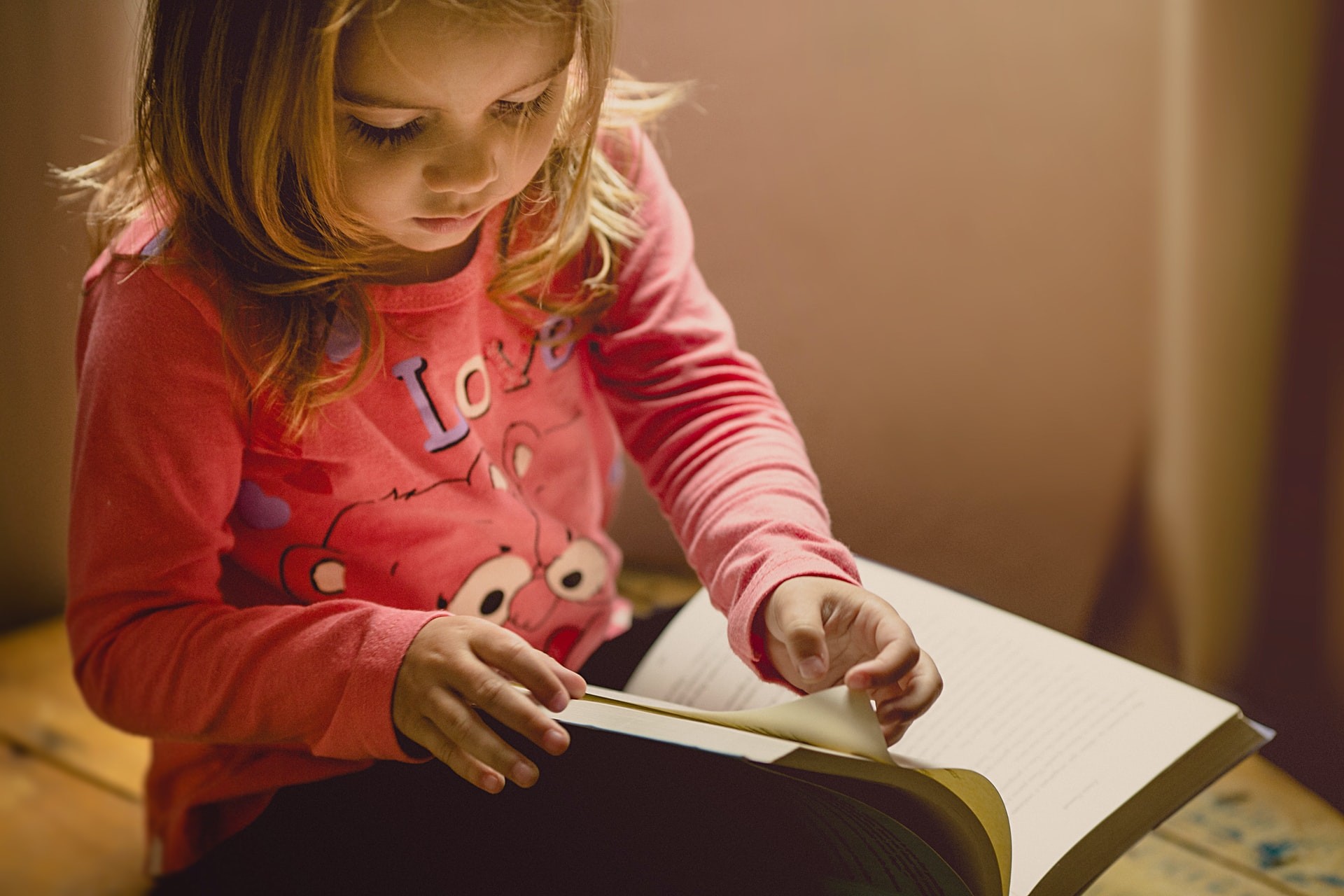 A young girl in a pink shirt reads a storybook to improve reading comprehension skills.