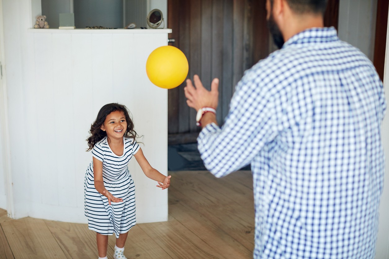 A father playing catch with his daughter indoors.