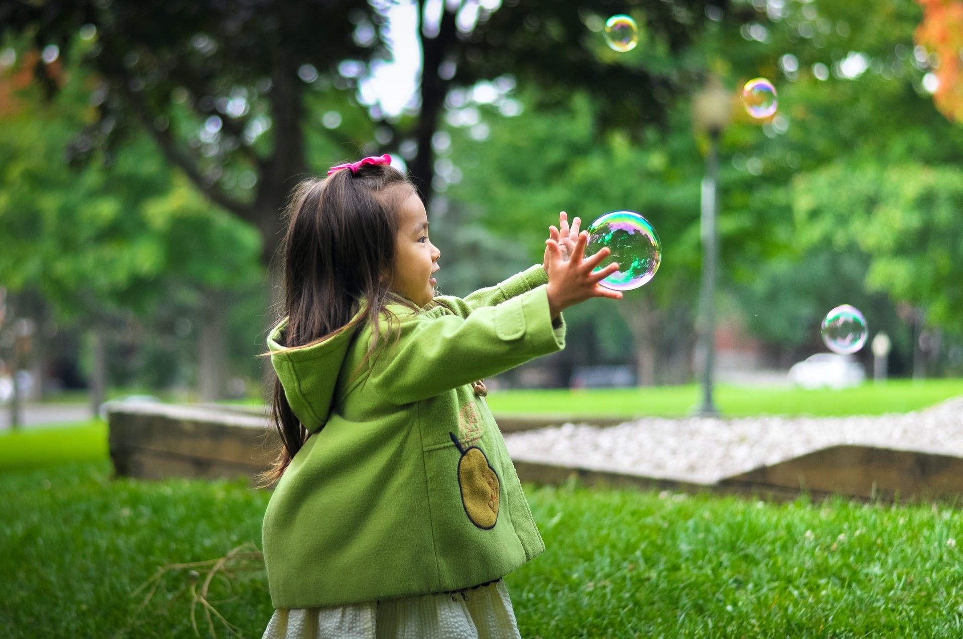 A young girl plays outside with bubbles to promote physical development through play-based learning activities.