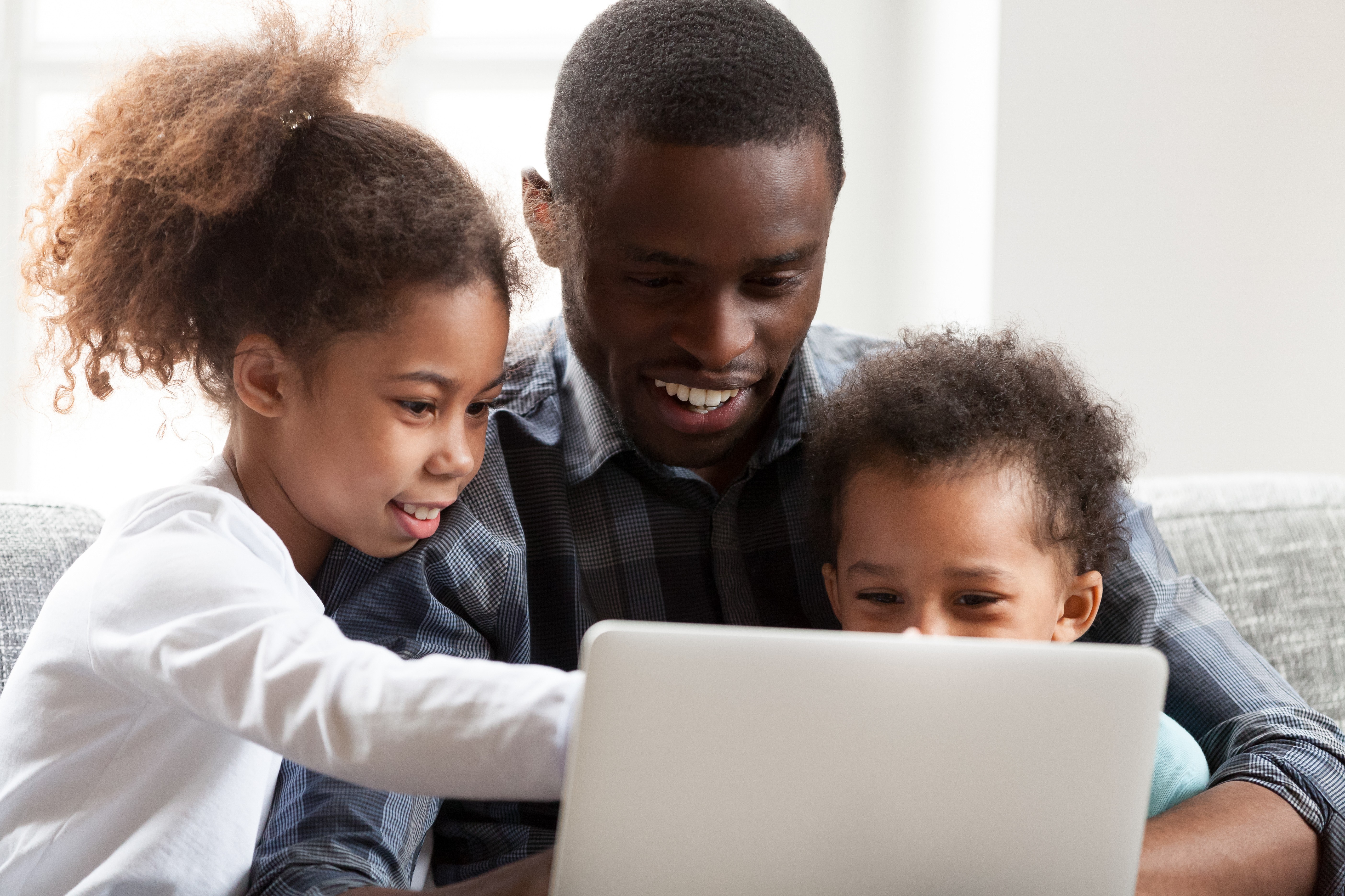 A happy parent sharing laptop with toddler and daughter.