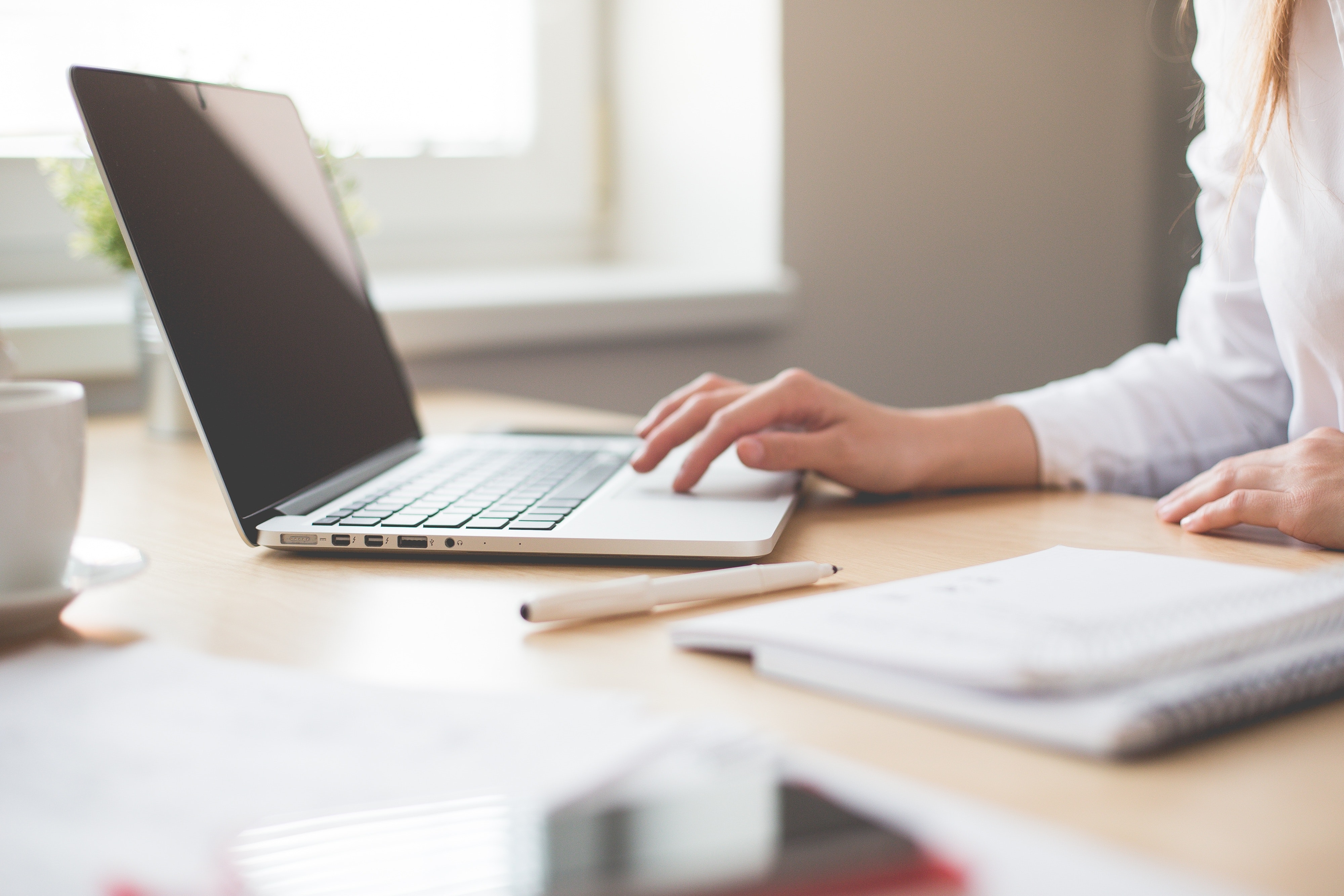 Woman working on laptop at table by window.
