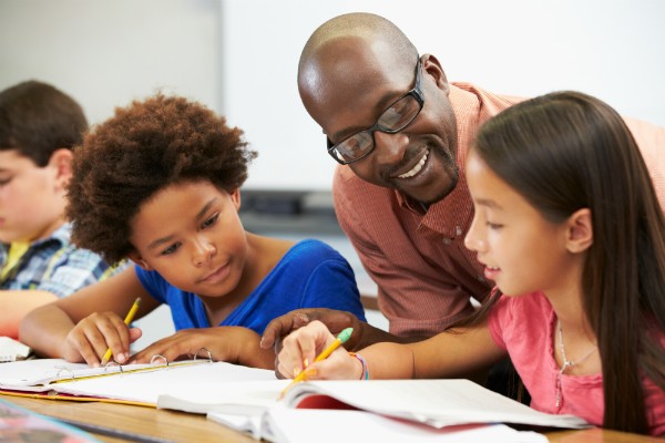 A teacher offers advice to a pair of students working together to complete a question.